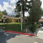 A yellow real estate house with a sloped lawn and trees