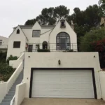 A two-story white real estate house with a gable roof, arched window, and large garage