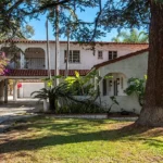two-story house with white walls colorful flowers, and a driveway.
